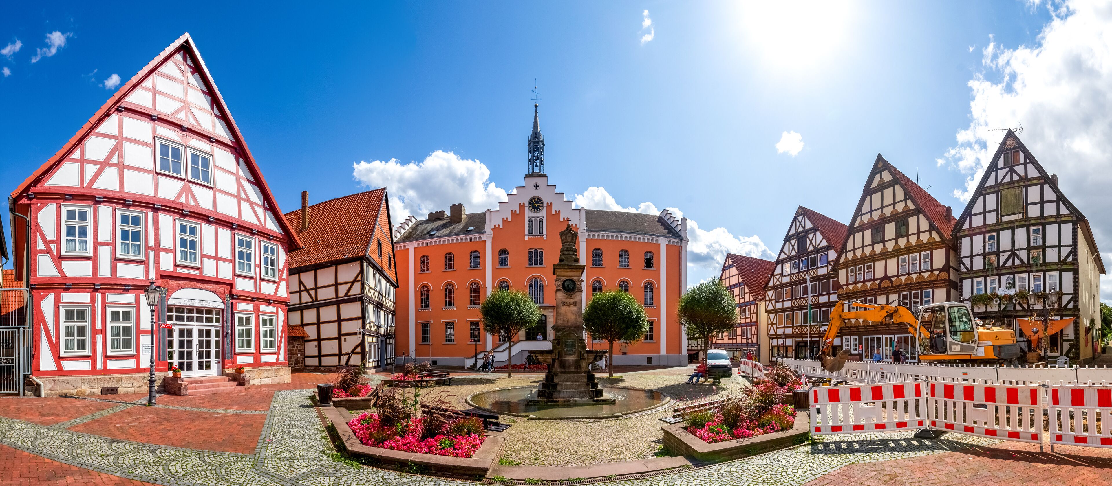 A historic town square with traditional half-timbered houses, a central fountain, and a church with a spire.