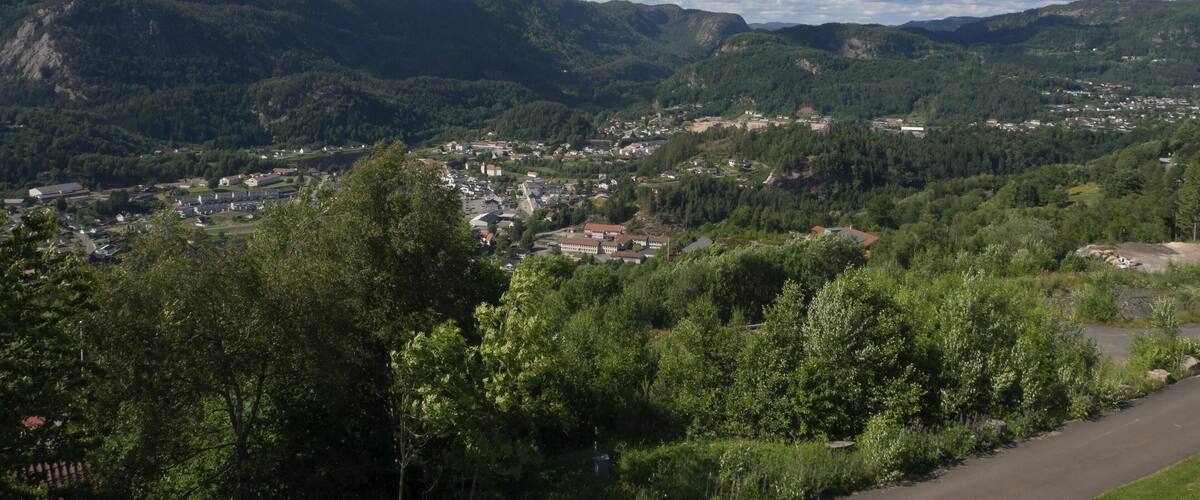 A mountainous landscape with a town nestled among the hills, a clear sky with scattered clouds, and lush greenery.