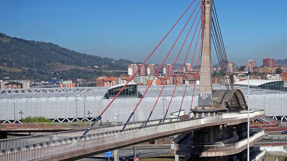 A modern bridge with red cables, a pedestrian walkway, and a road with directional signs.
