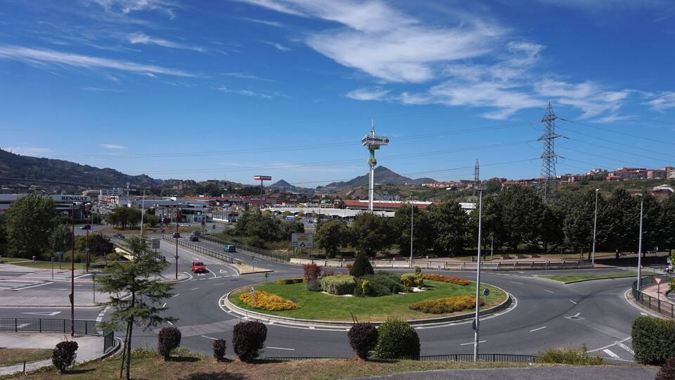 A roundabout with a central landscaped area, surrounded by roads, buildings, and a mountainous backdrop.