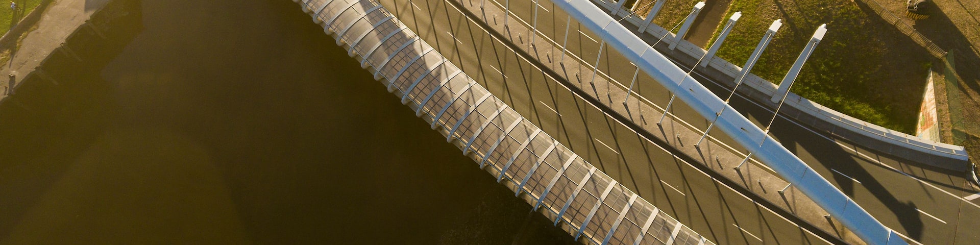 A bridge with a curved design spanning over a body of water, surrounded by greenery and urban infrastructure.