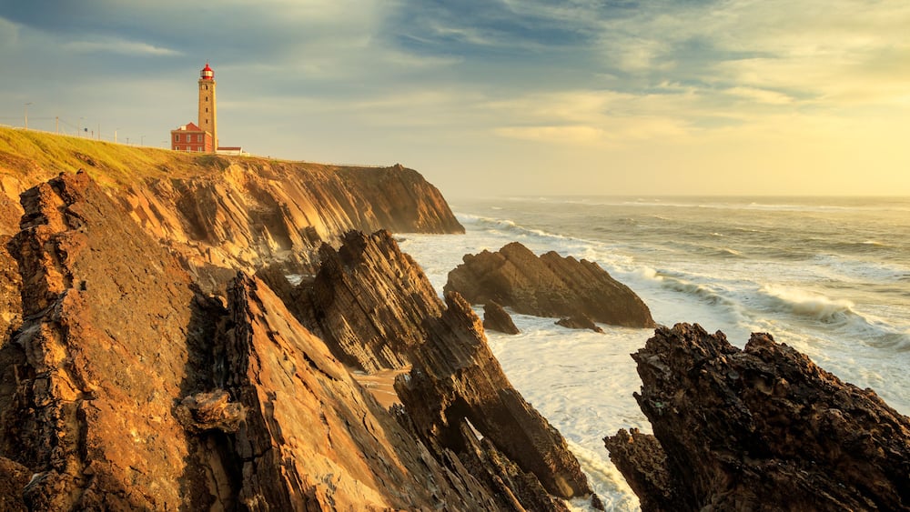 A coastal landscape with a lighthouse, rocky cliffs, and the ocean.
