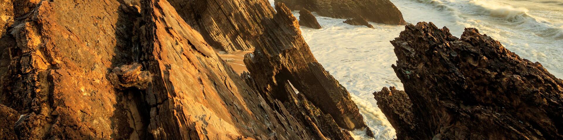 A coastal landscape with a lighthouse, rocky cliffs, and the ocean.