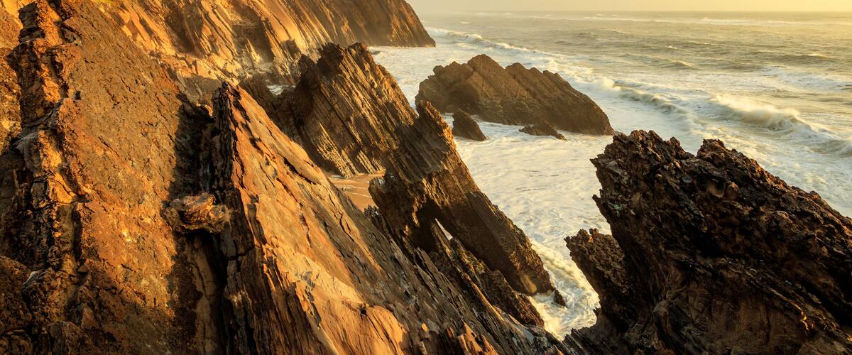 A coastal landscape with a lighthouse, rocky cliffs, and the ocean.