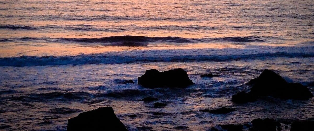 A sunset over the ocean with waves and rocks in the foreground.