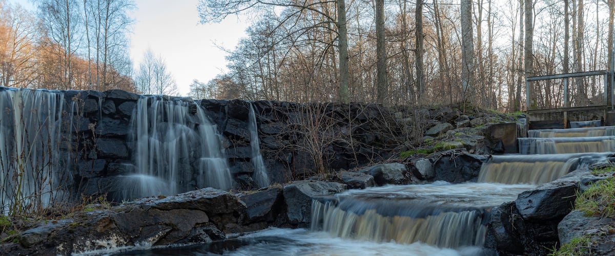 A multi-tiered waterfall in a forested area with rocky terrain and bare trees.