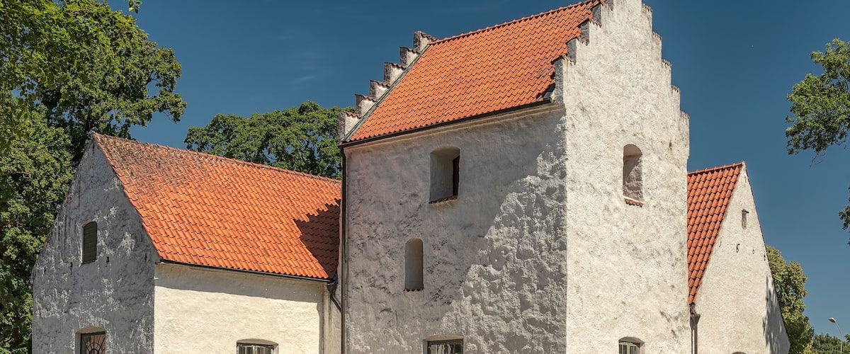 Een historisch gebouw met een rode pannendak en witte muren, omgeven door bomen.