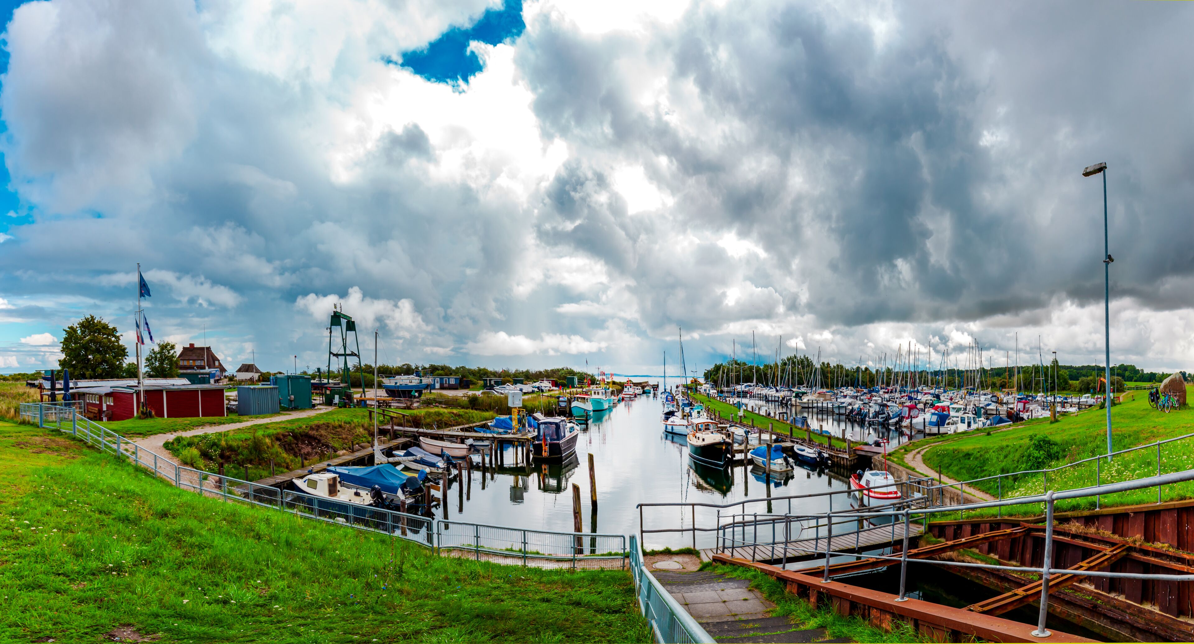 A marina with boats docked, a grassy area, and a cloudy sky.