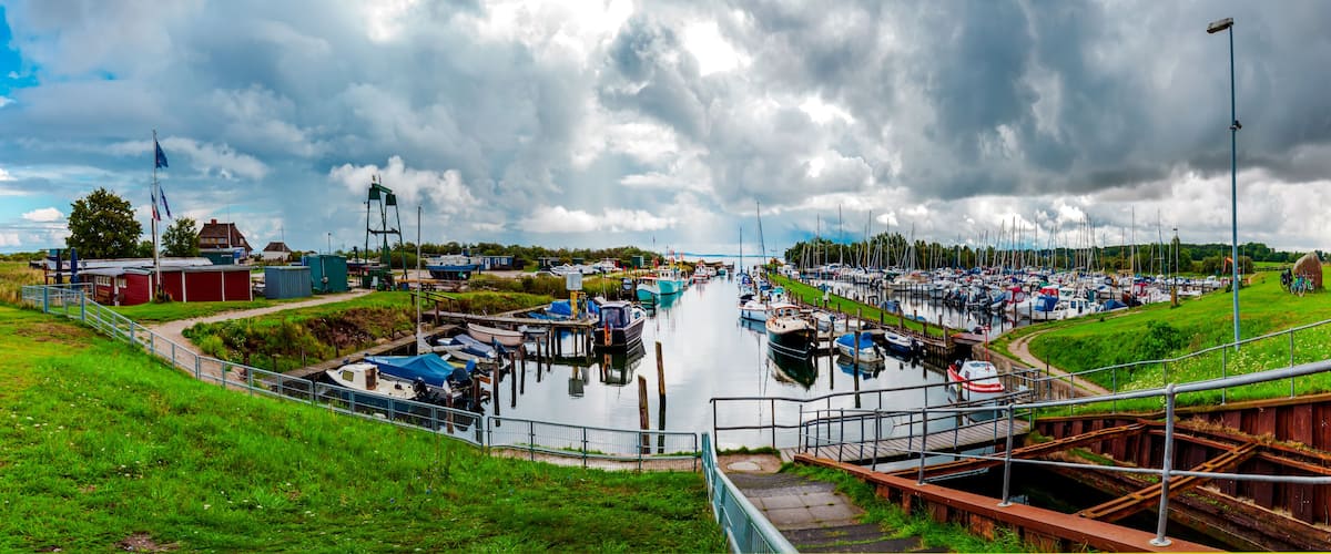 A marina with boats docked, a grassy area, and a cloudy sky.