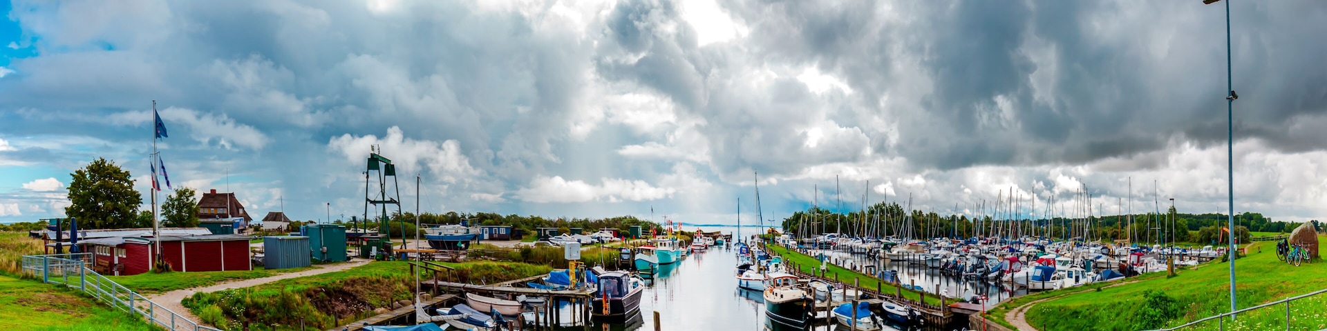 A marina with boats docked, a grassy area, and a cloudy sky.