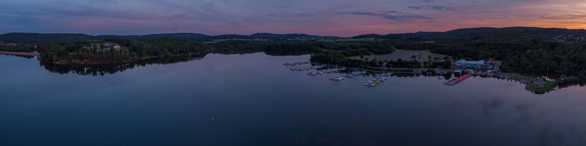 A calm lake with a marina and boats, surrounded by hills and trees.
