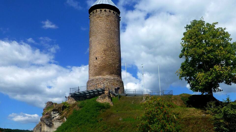 A stone tower with a conical roof, surrounded by greenery and a clear sky.