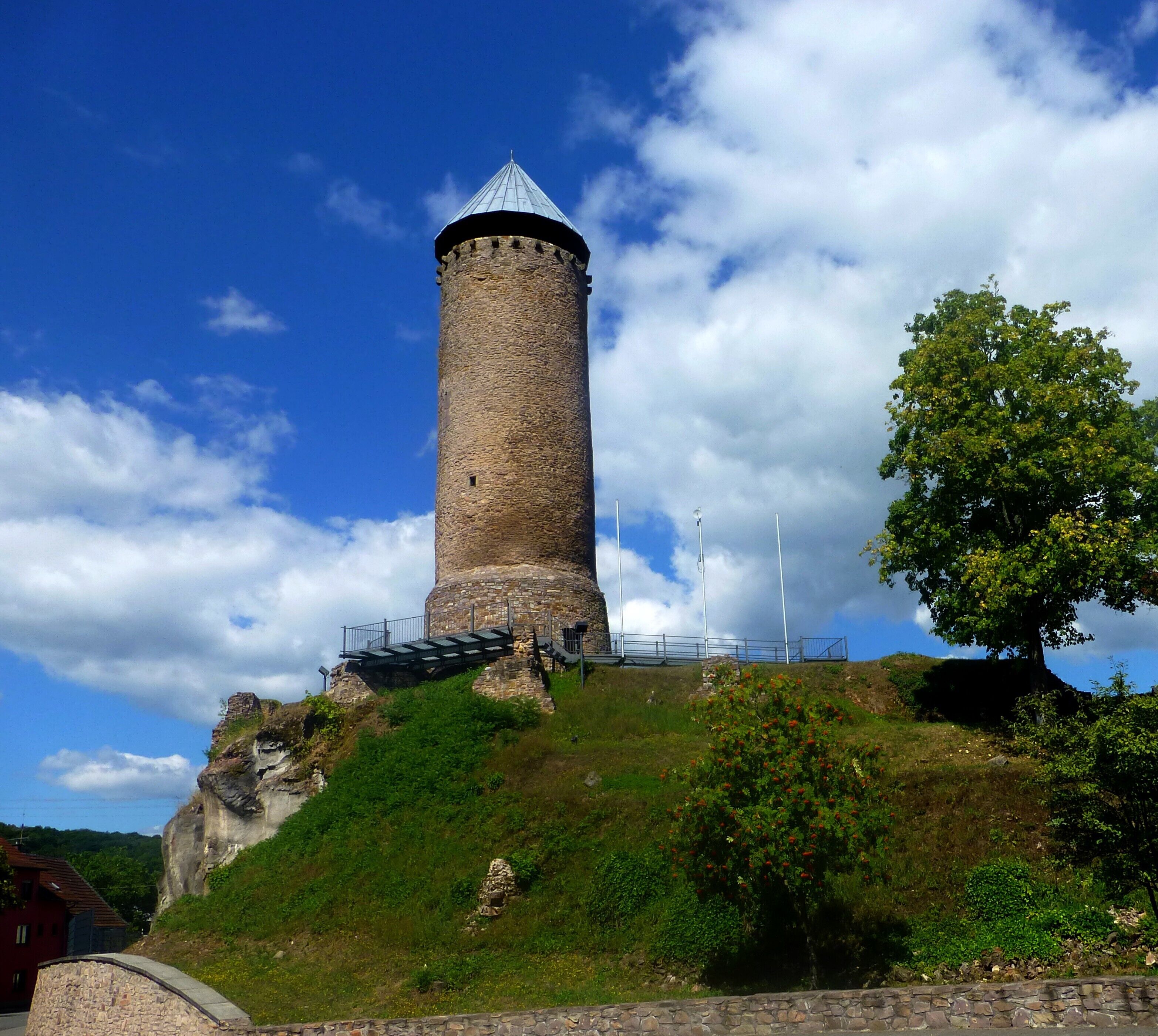 A stone tower with a conical roof, surrounded by greenery and a clear sky.