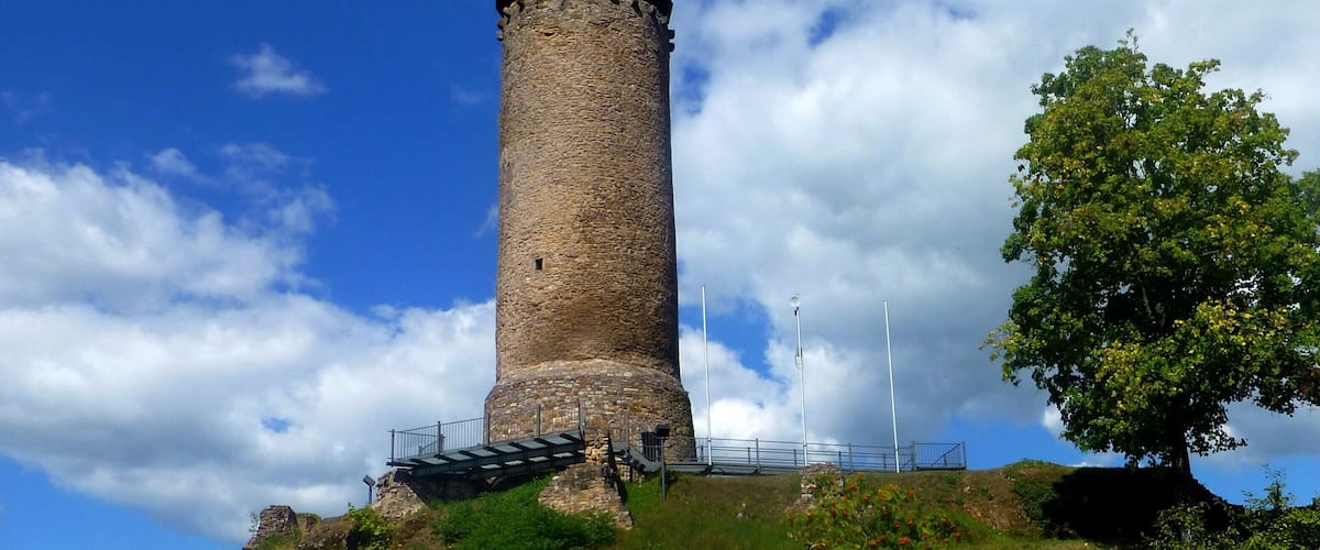 A stone tower with a conical roof, surrounded by greenery and a clear sky.