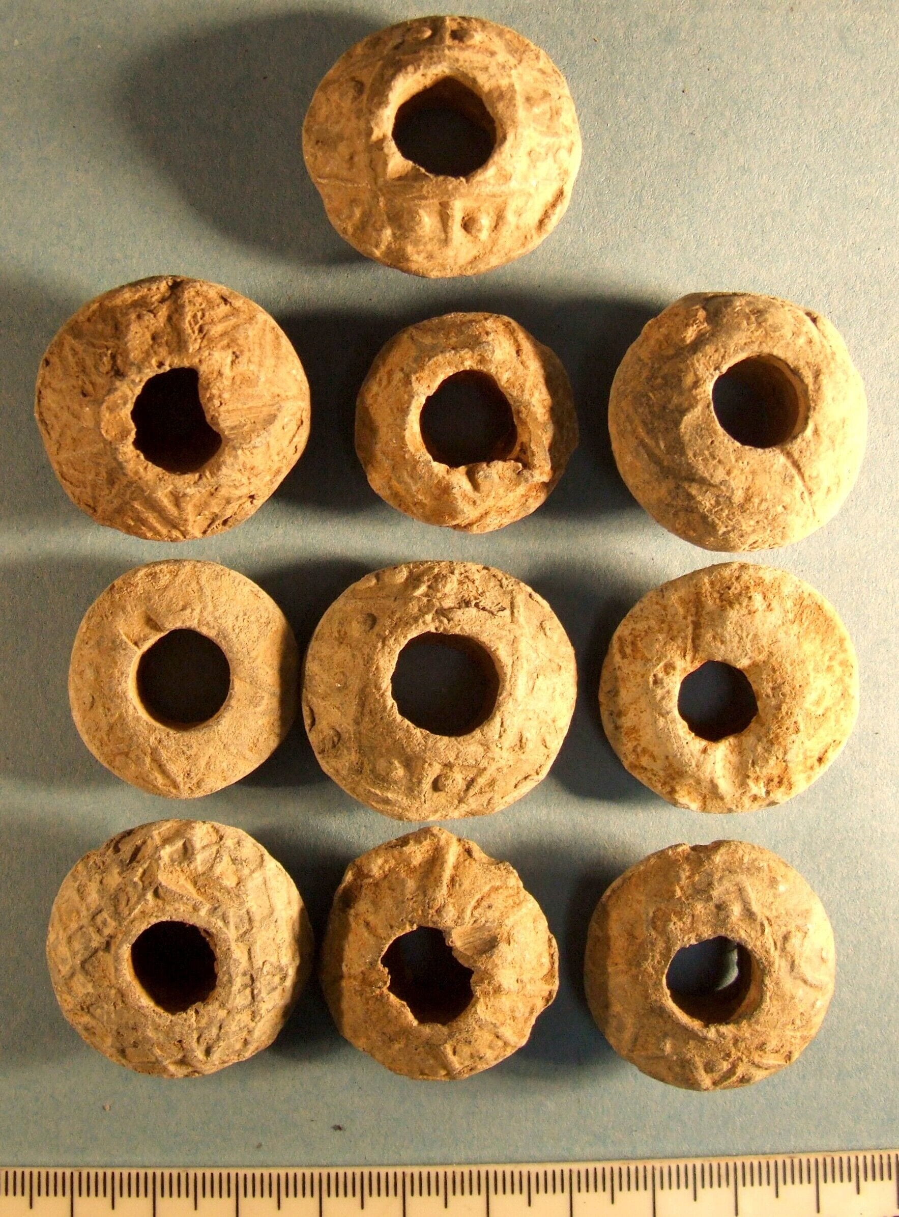 10 cast lead biconical spindle whorls. From top left to bottom right: 1. D:31mm. Decorated with zig-zag line with pellet in each angle. 2: D:29mm. Decorated with double zig-zag motif 3: D:24mm. Decorated with zig zag motif 4: D:29mm. Undecorated 5: D:26mm. Decorated with zig-zag line with pellet in each angle 6: D:31mm. Decorated with zig-zag line with pellet in each angle 7: D:29mm. Decorated with zig-zag line with pellet in each angle 8: D:30mm. Decorated with net motif 9: D:27mm. Decorated with transverse lines with two or three pellets between 10: D:29mm. Decorated with zig-zag line with pellet in each angle