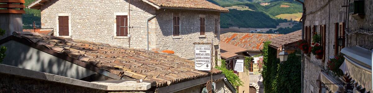 Eine enge Gasse mit traditionellen Steinbauten, einem Schild und einer bergigen Landschaft im Hintergrund.