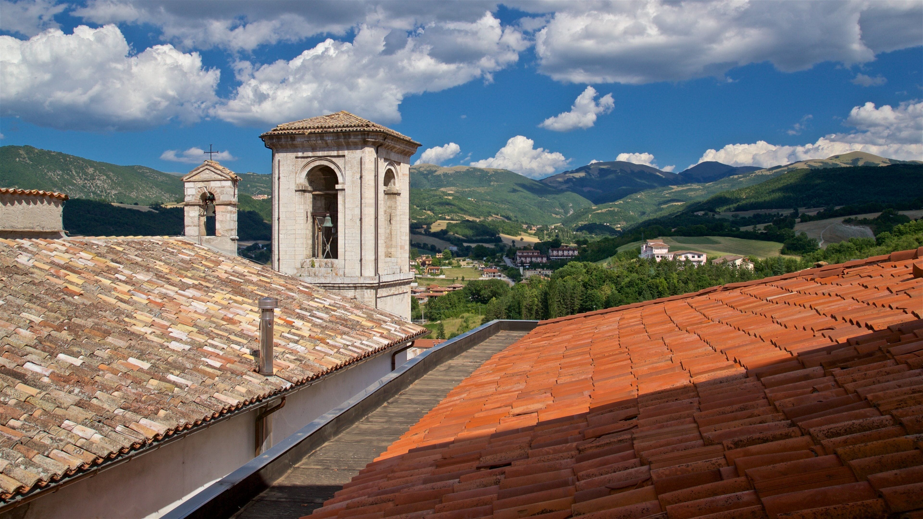 A church with a bell tower and a tiled roof overlooking a valley with mountains.