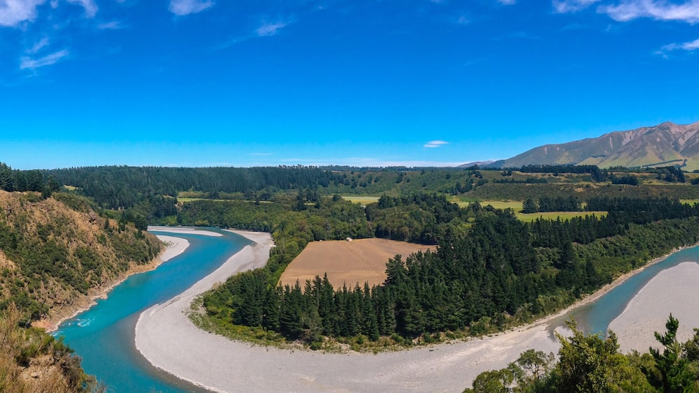 Ein Fluss schlängelt sich durch ein Tal, im Hintergrund ein Berg.
