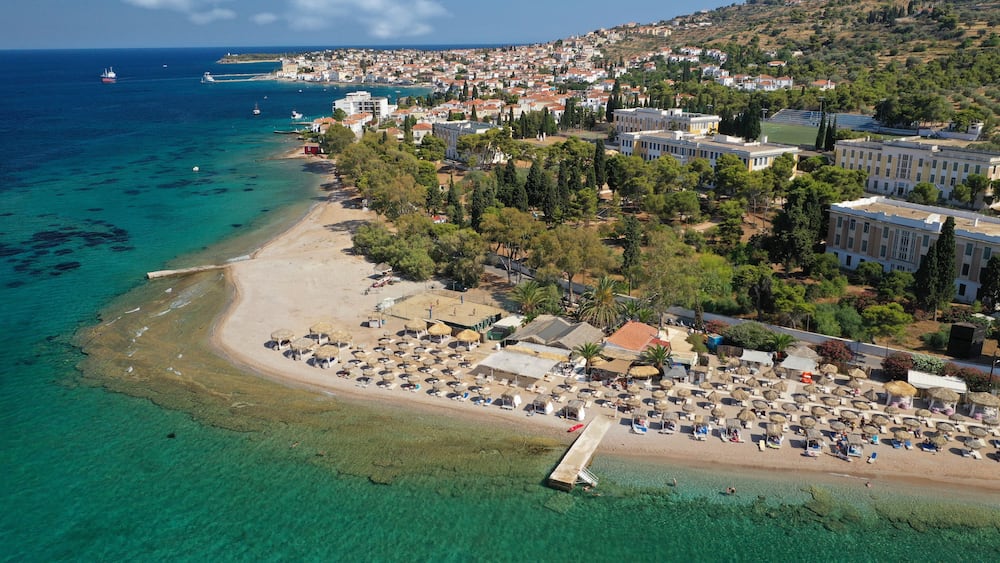 A coastal town with a beach, clear turquoise waters, and a mix of residential and commercial buildings.