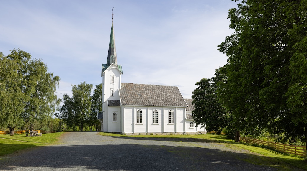 A white church with a tall steeple and a gravel driveway leading to it.