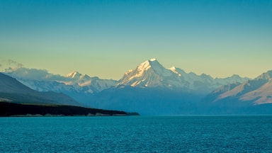 Una cordillera con un pico destacado, un lago tranquilo y una costa boscosa.