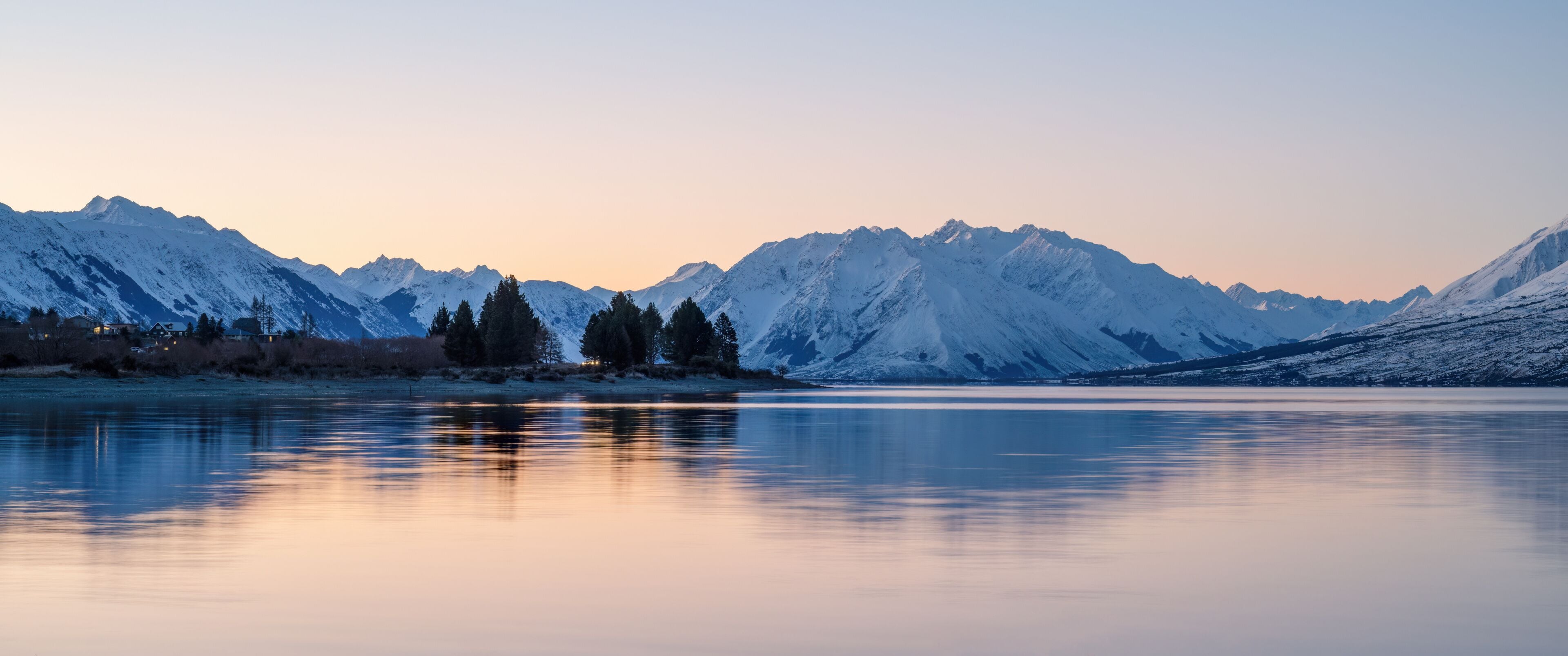 A calm lake reflecting snow-capped mountains during twilight.