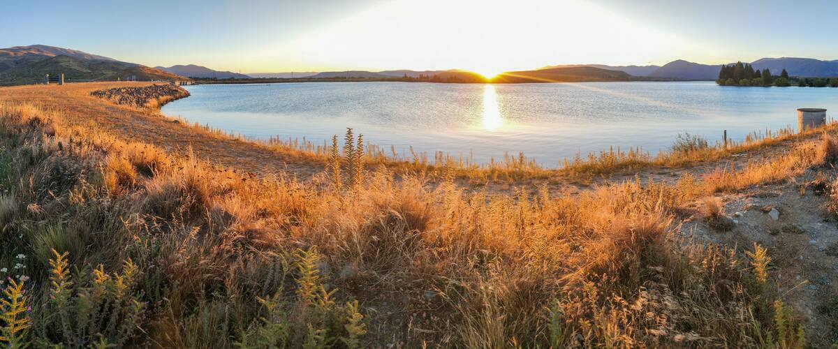 A lake surrounded by dry grass and mountains in the background.