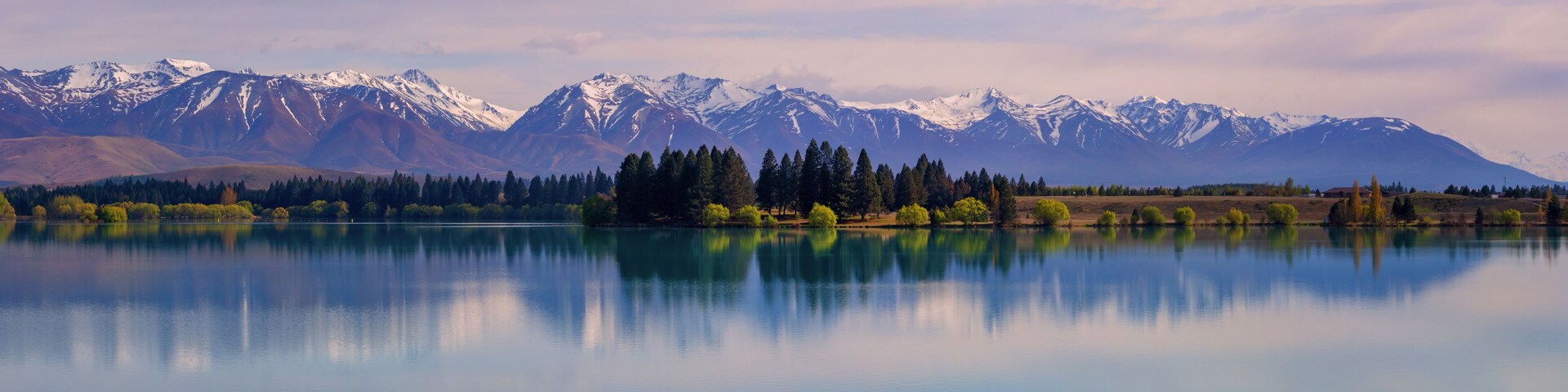 Um lago tranquilo refletindo montanhas e árvores.