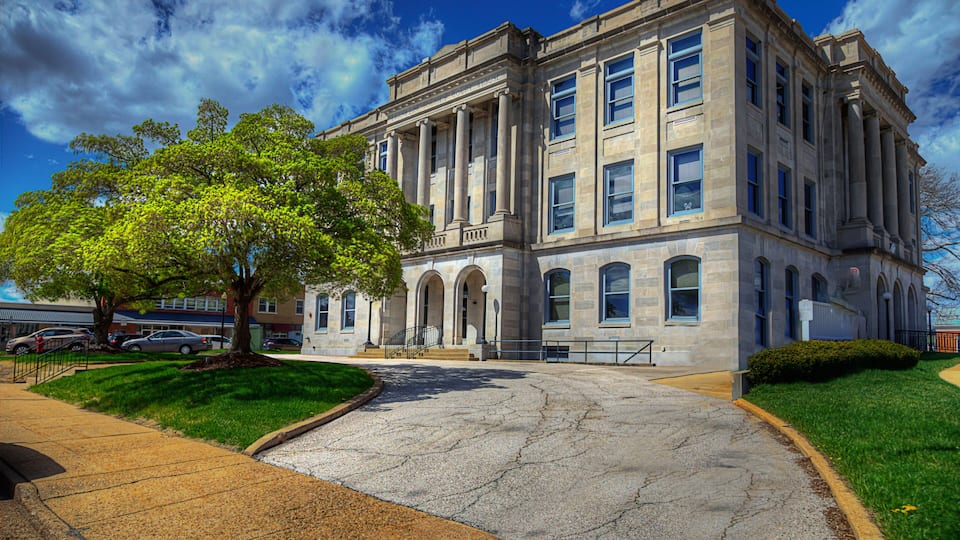 A large stone building with columns, a tree in front, and a clear blue sky.