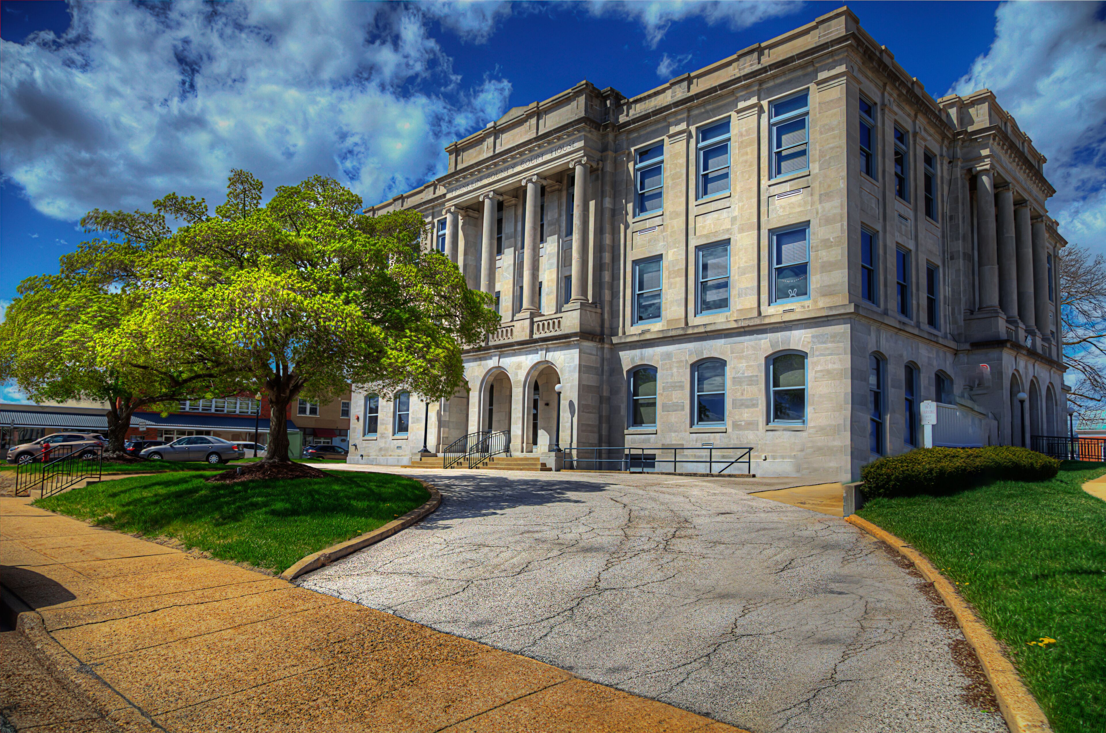 A large stone building with columns, a tree in front, and a clear blue sky.