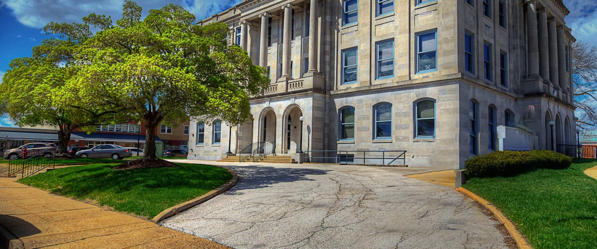 A large stone building with columns, a tree in front, and a clear blue sky.