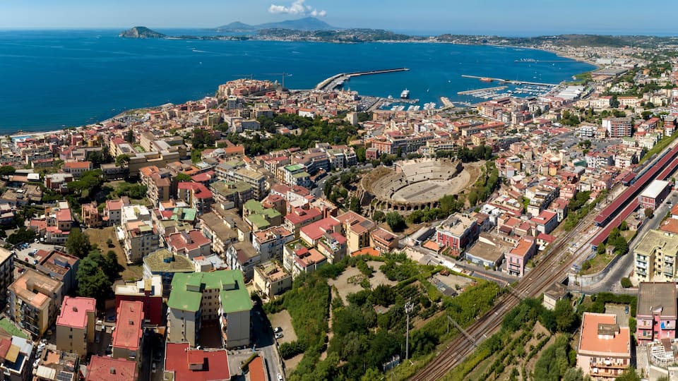 A coastal cityscape with a prominent waterfront, a large stadium, and a railway line.