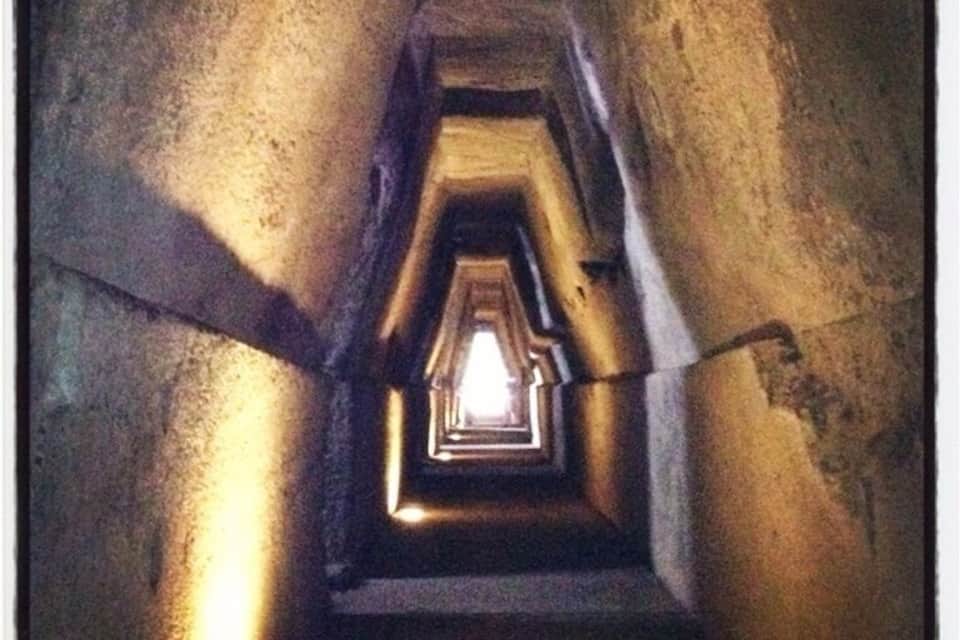Una estrecha escalera de piedra, tenuemente iluminada, que asciende entre paredes de piedra tosca.