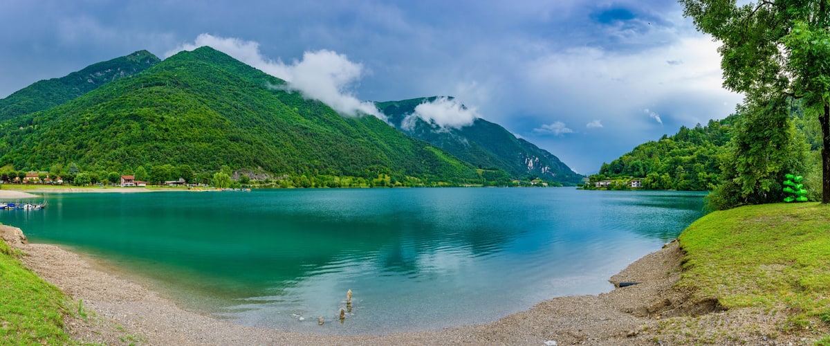 A lake surrounded by lush green hills and a mountain with a small building on its peak.