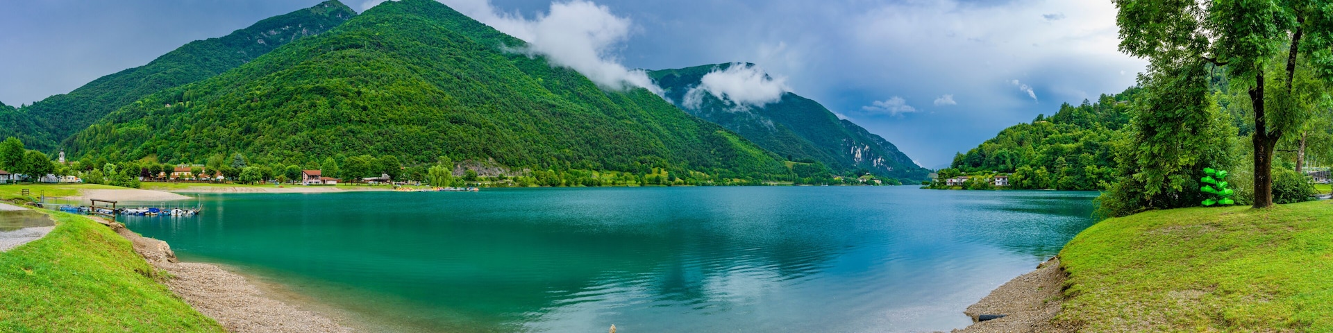 A lake surrounded by lush green hills and a mountain with a small building on its peak.