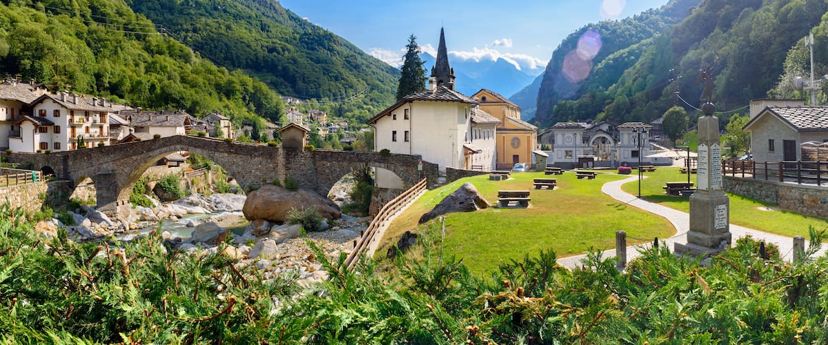 A picturesque village with a stone bridge, lush green mountains, and traditional buildings.