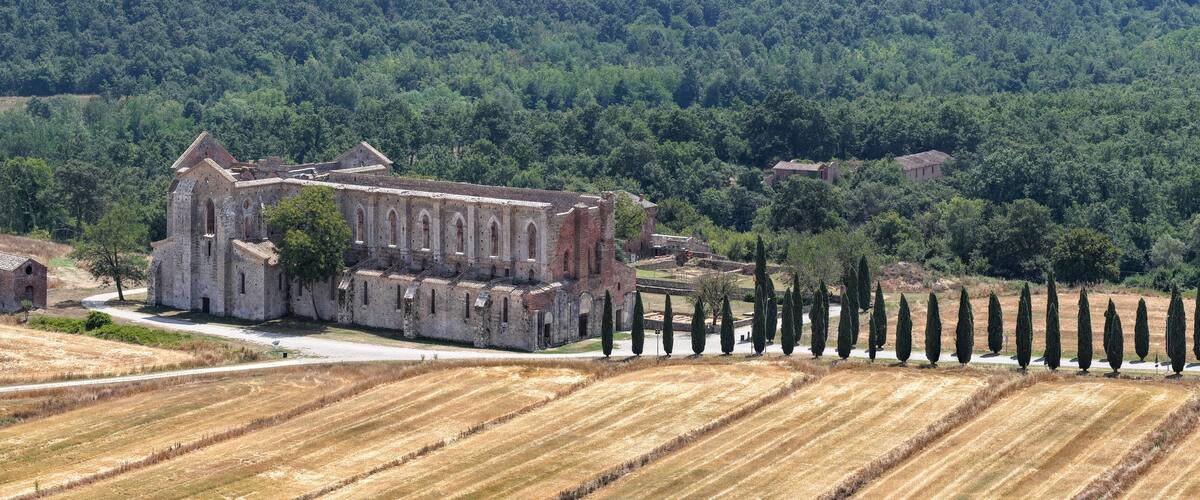 An ancient stone church surrounded by fields and forest.