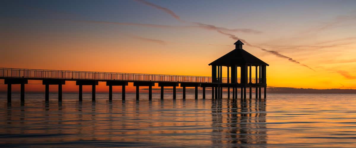A pier extending into calm waters at sunset with a gazebo on the end.