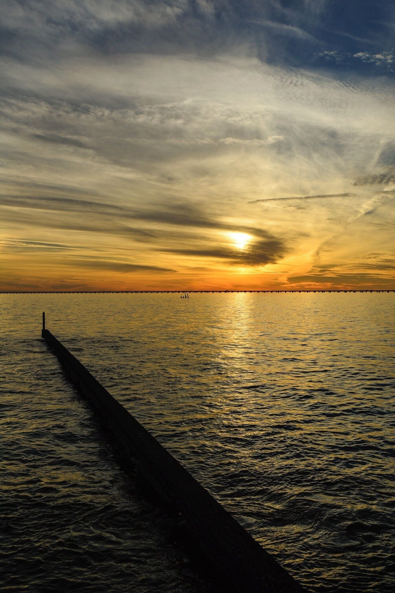 A sunset over a calm sea with a pier extending into the water.