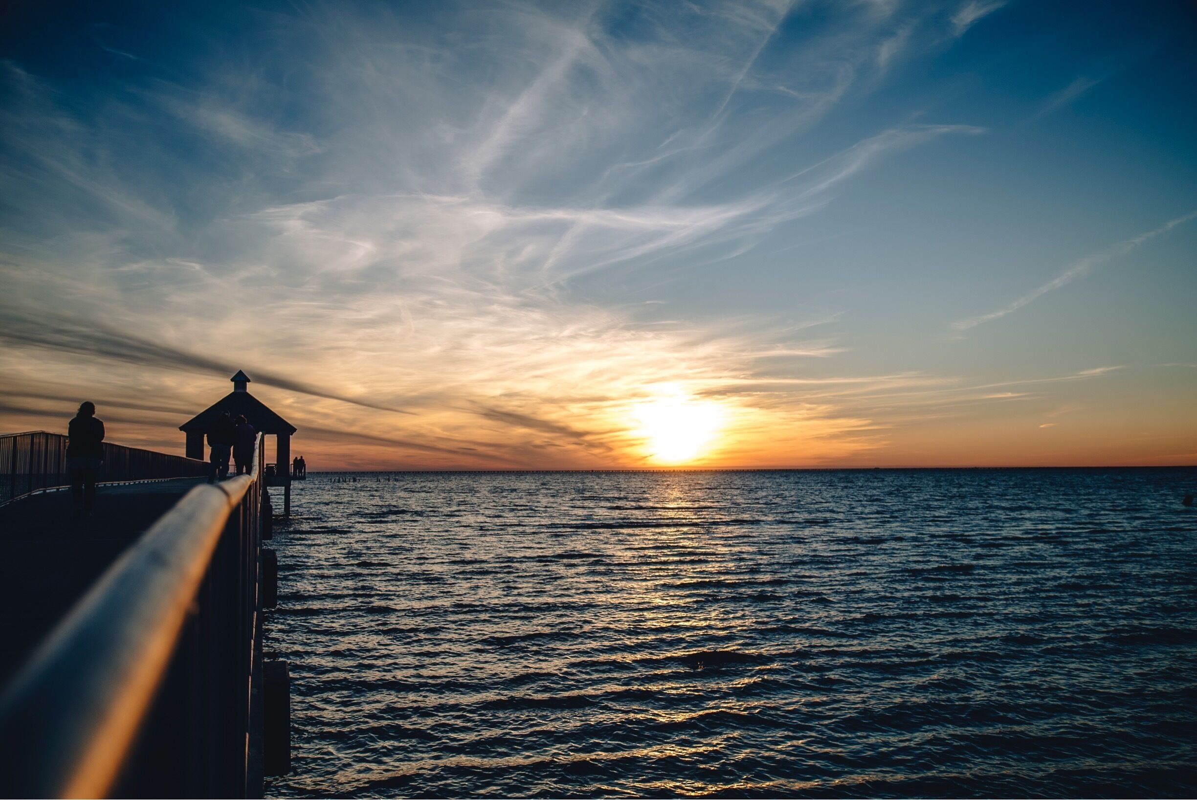 Un muelle que se adentra en el océano al atardecer, bajo un cielo despejado.