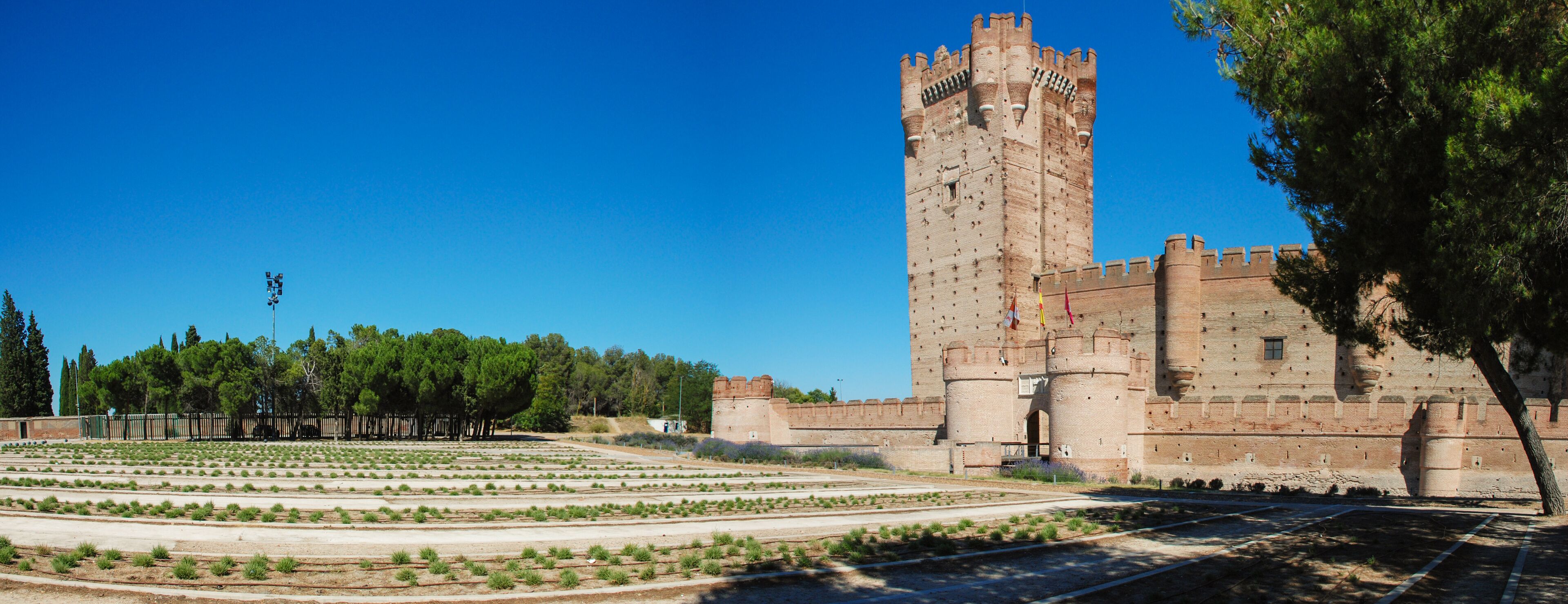 A historic castle with a tall tower, surrounded by a landscaped garden and trees.