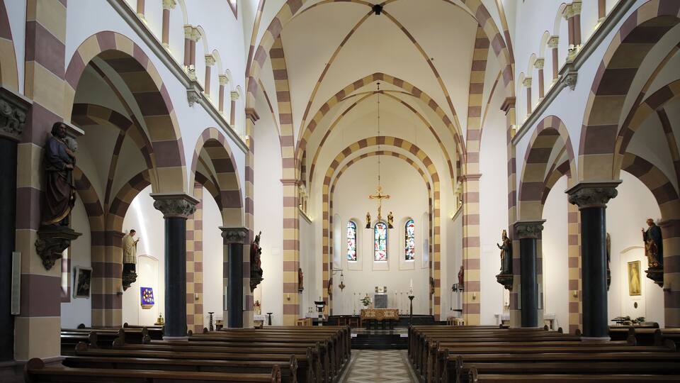 An interior of a church with arched ceilings, wooden pews, and stained glass windows.