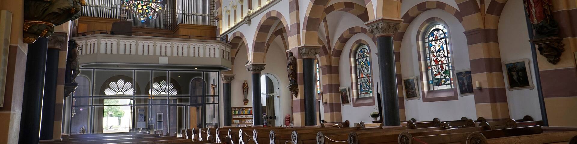 An interior of a church with arched ceilings, stained glass windows, and wooden pews.