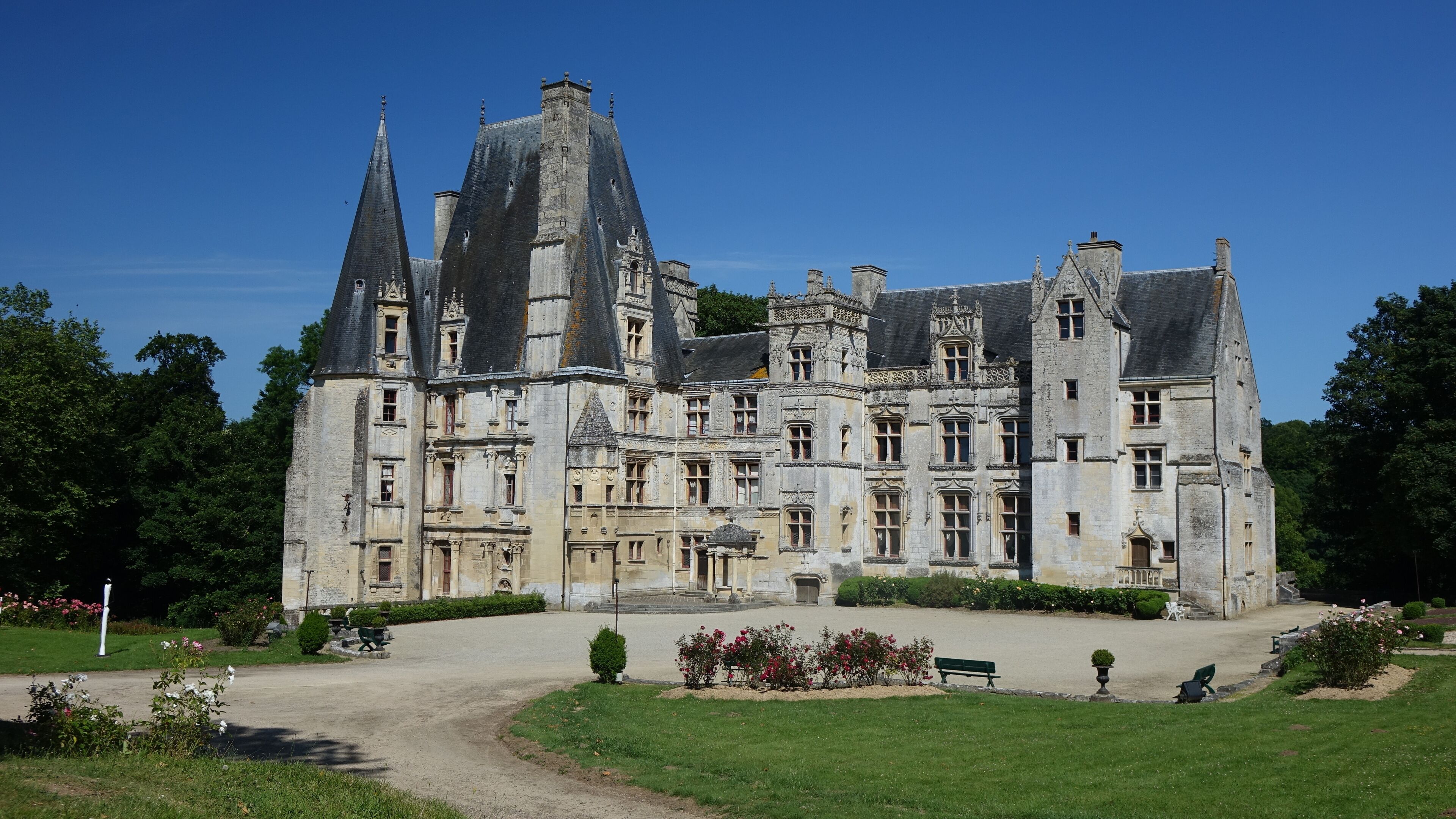 A large, historic château with multiple towers and a well-maintained garden.