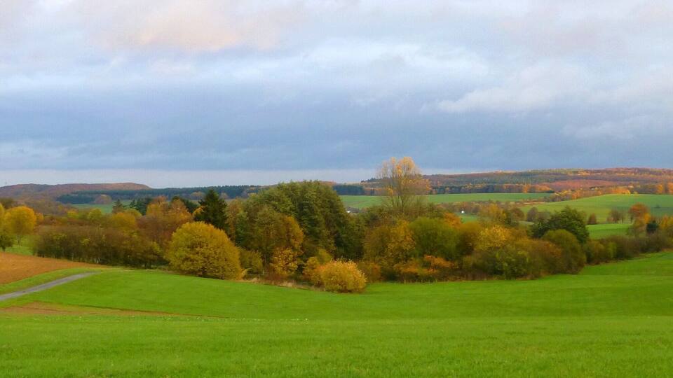 A rural landscape with rolling hills, a church, and autumn-colored trees.