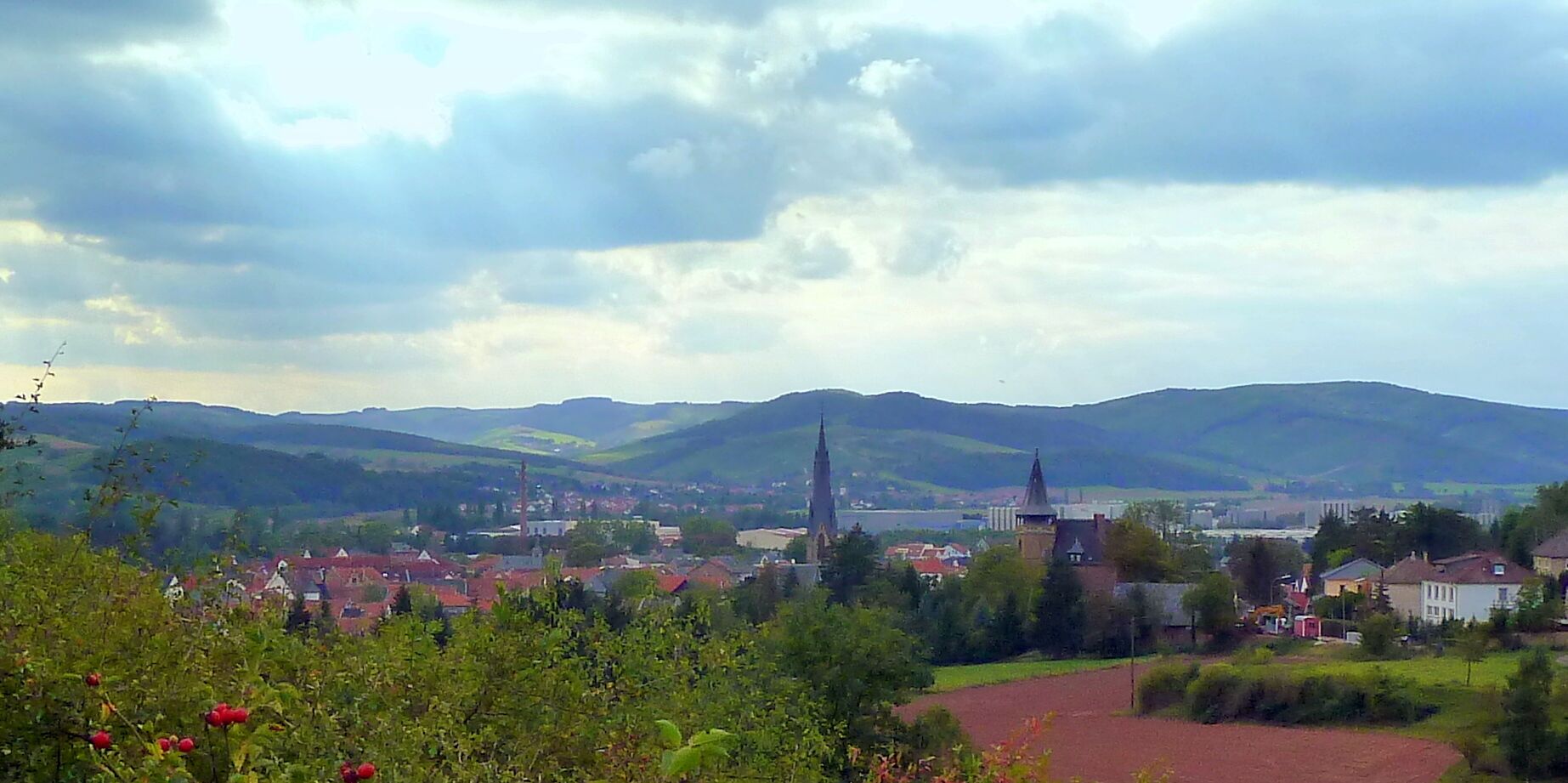 A town with a prominent church spire, surrounded by rolling hills and a river.