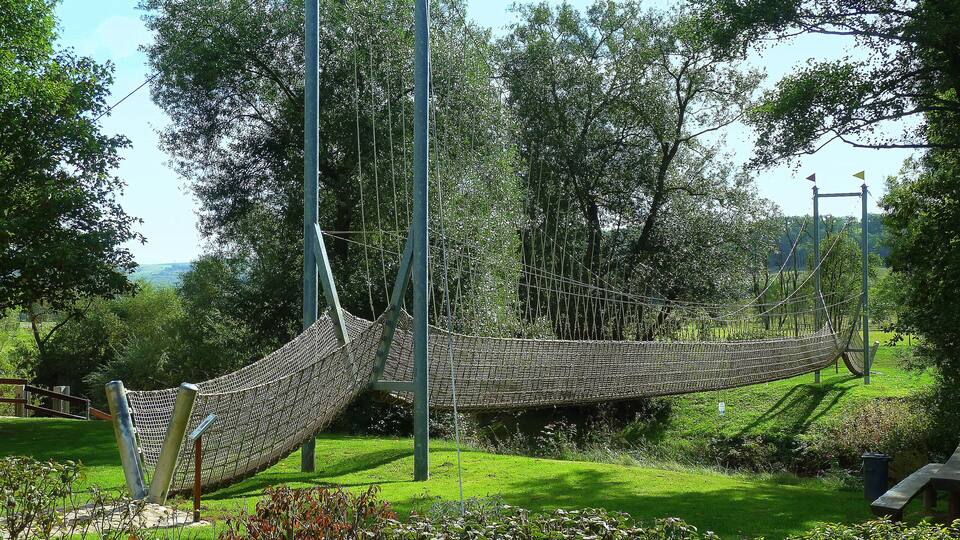 A rope bridge in a park with green grass and trees.