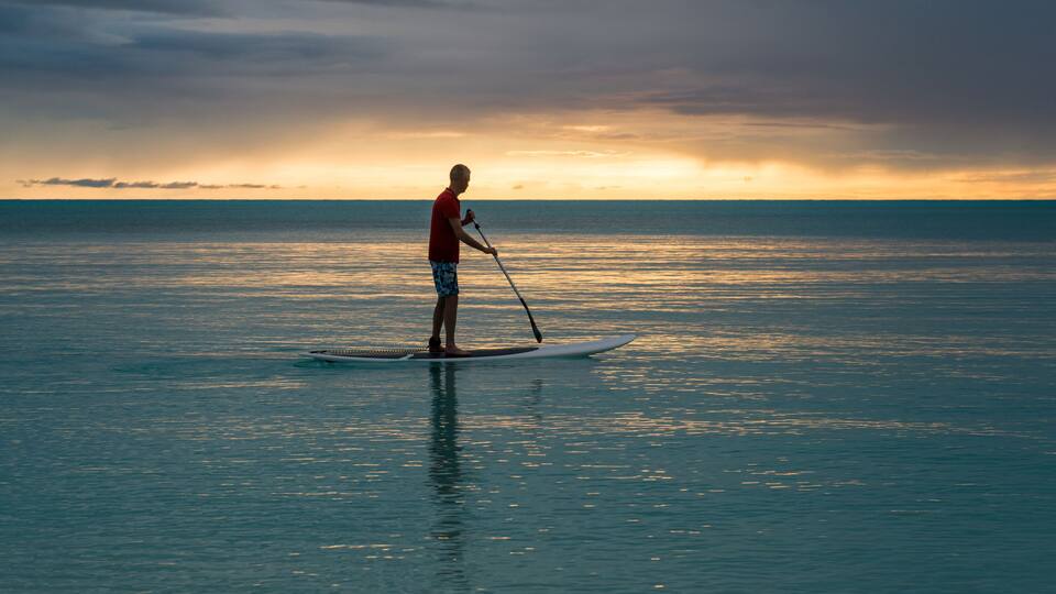 A person paddleboarding on calm ocean waters during sunset.