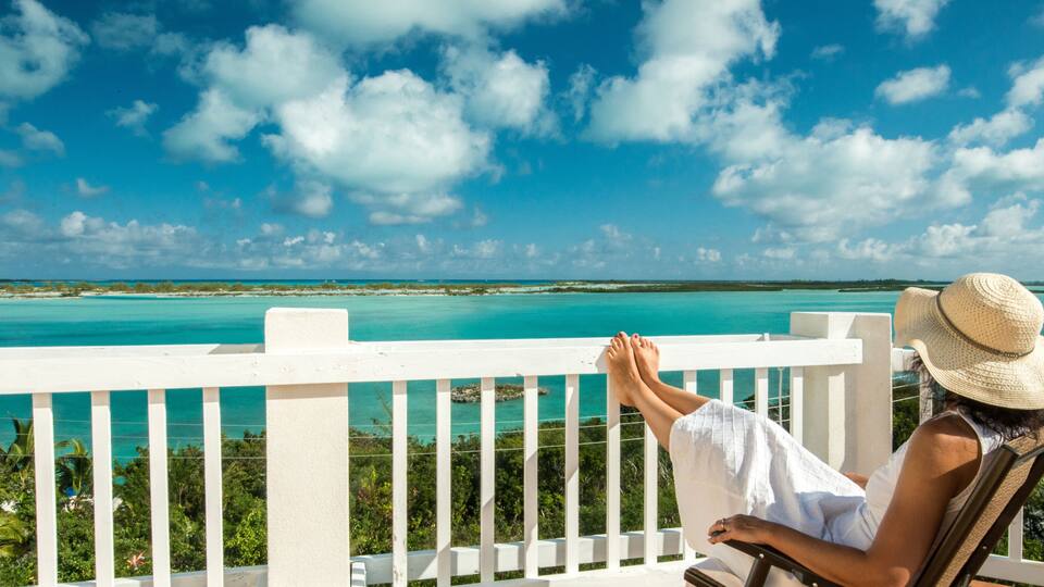 A person relaxing on a balcony with a view of turquoise waters and a clear sky.