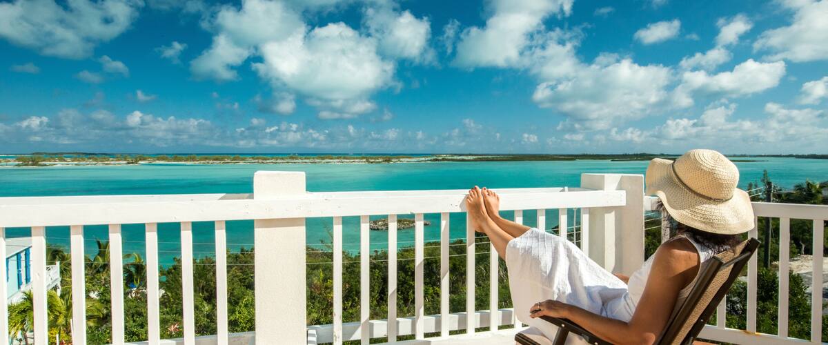 A person relaxing on a balcony with a view of turquoise waters and a clear sky.